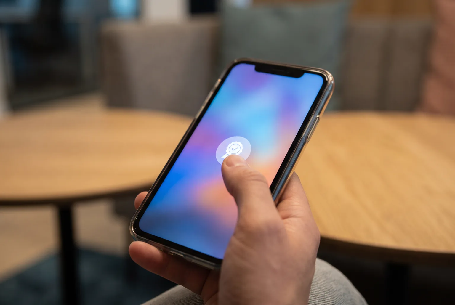 A thumb tapping a rounded badge button on a smartphone screen glowing with a soft blurred gradient
